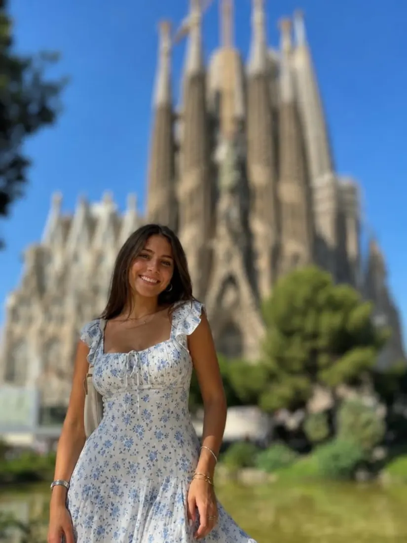 A woman in a blue floral dress stands before the Sagrada Familia, before the Background Enhancer improves the backdrop.