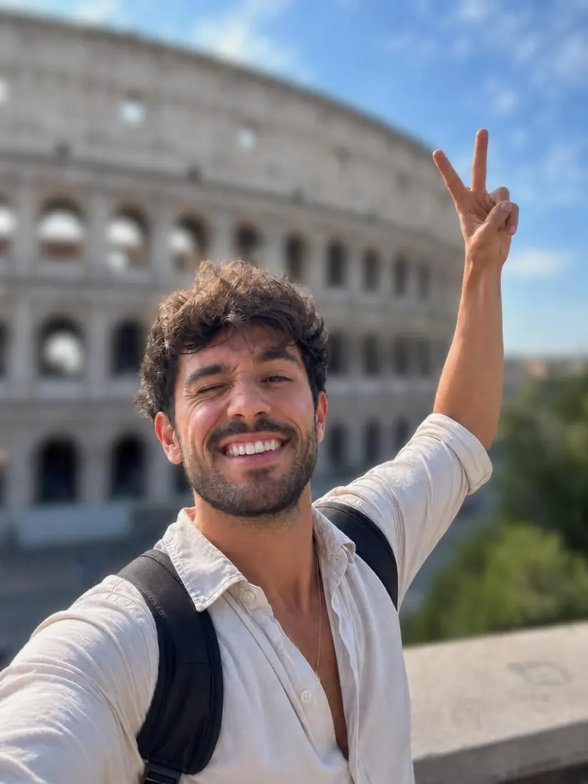 A man in an open white shirt and backpack makes a peace sign in front of the Colosseum, before the Background Enhancer improves the backdrop.