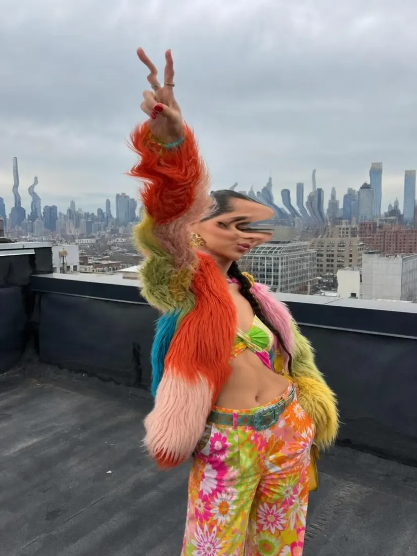 A woman in a rainbow faux-fur coat stands on a rooftop with her face and the skyline warped, before the Distortion Remover repairs the image.
