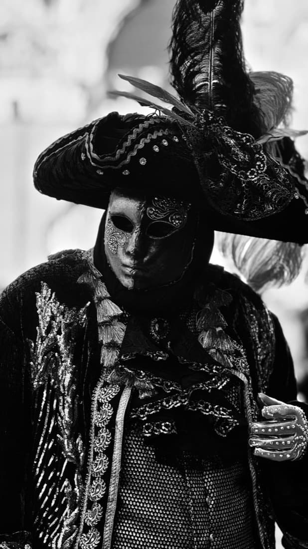 A black-and-white photo shows a Venetian carnival performer in an ornate mask costume, before the Image Colorizer adds color.