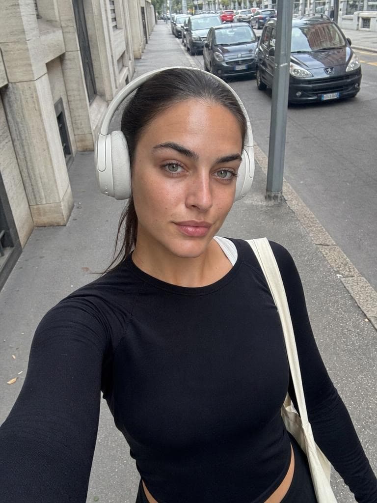 A woman in headphones and a black top takes a street selfie, before the Live Broadcast Generator restyles the scene.