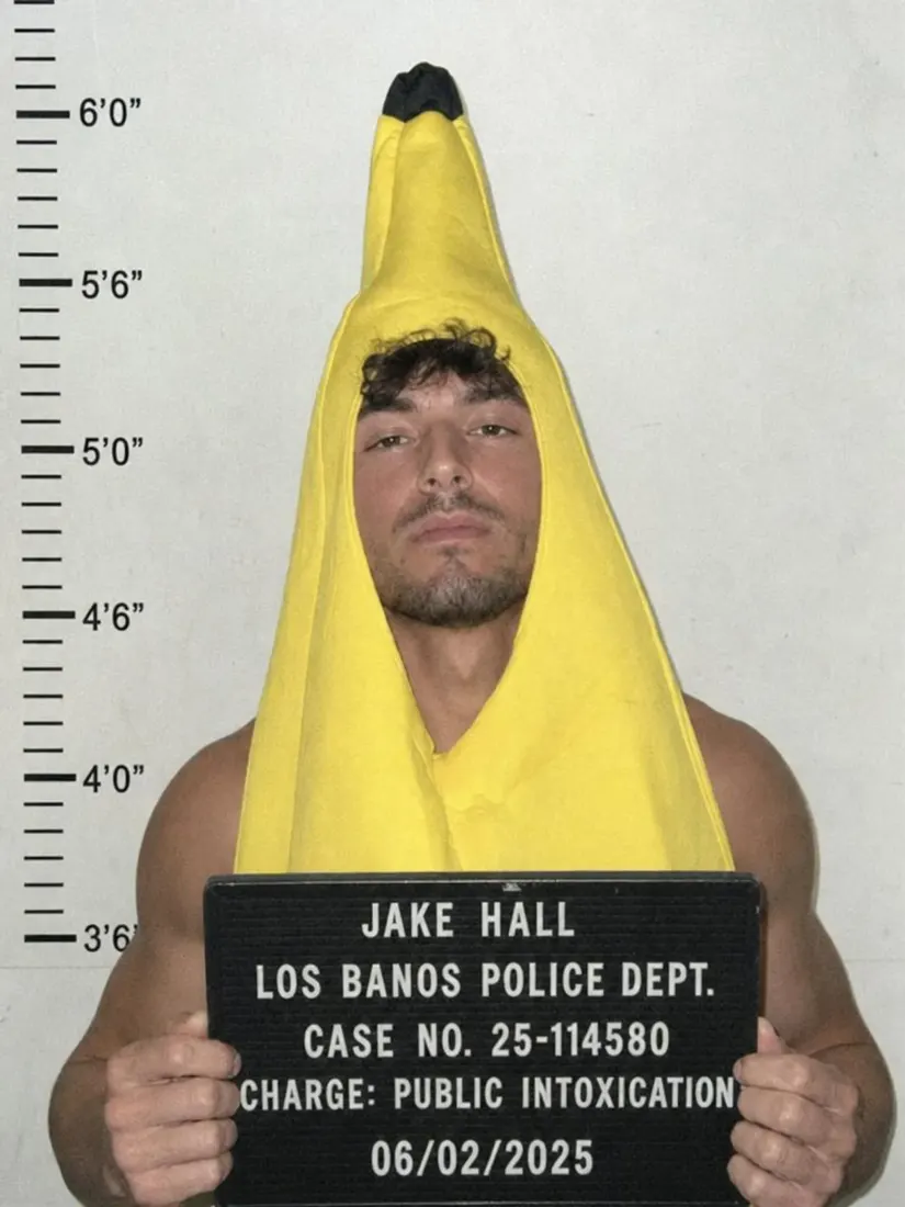 A man in a banana costume poses against a height chart with a fictional booking placard from the Mugshot Filter tool.