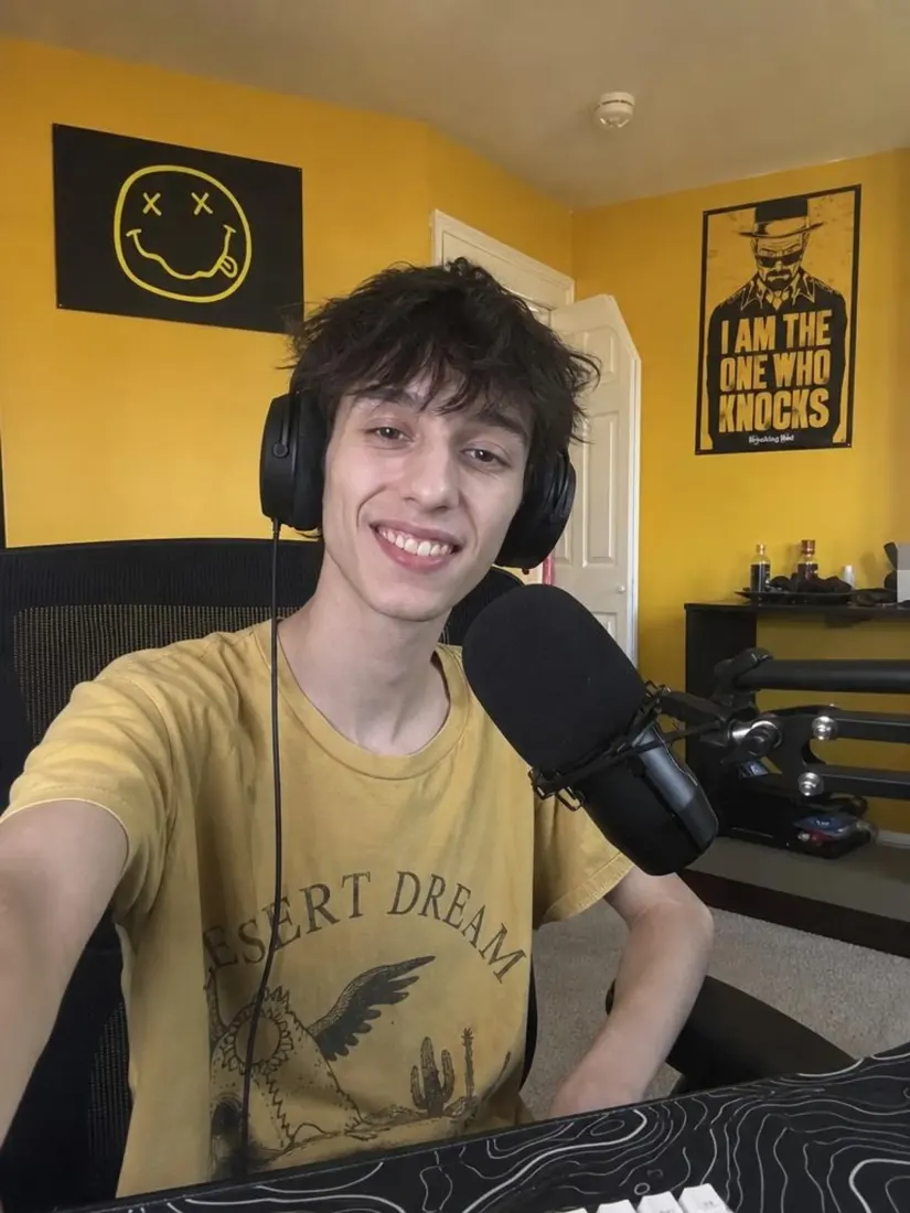 A slimmer young man in a yellow graphic tee sits in a yellow bedroom, before the Muscle Filter builds his physique.