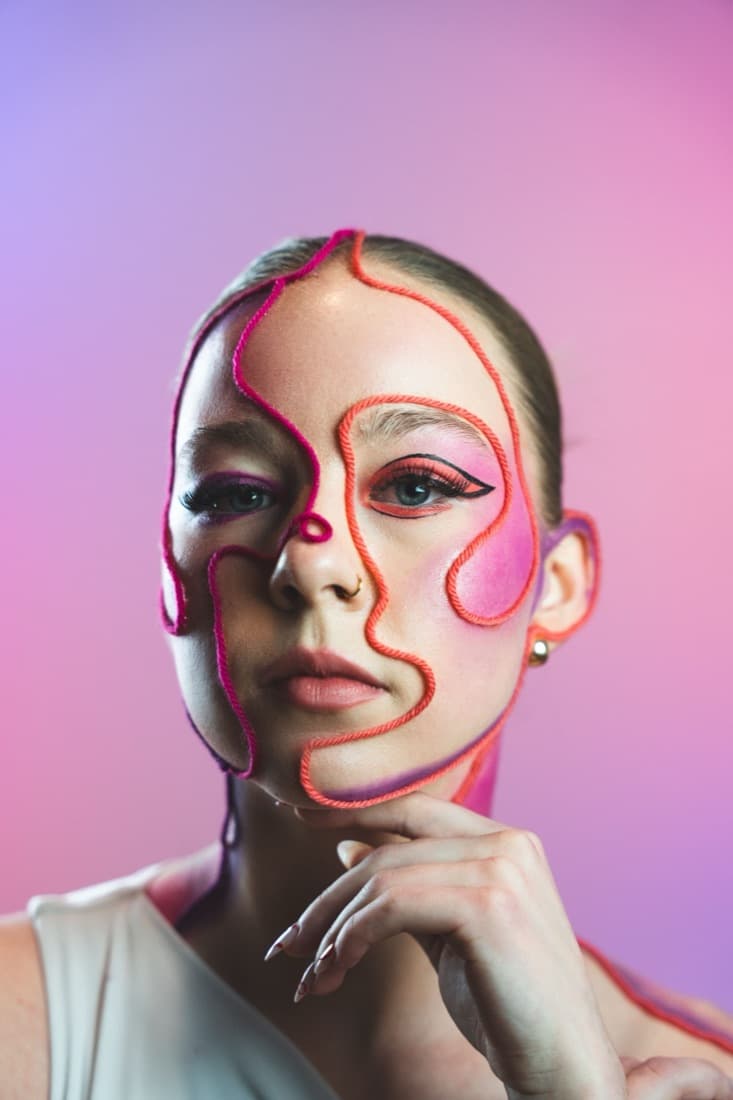 A woman poses with graphic face-paint lines drawn on her skin, before the Polygonal Art Generator turns it into faceted art.