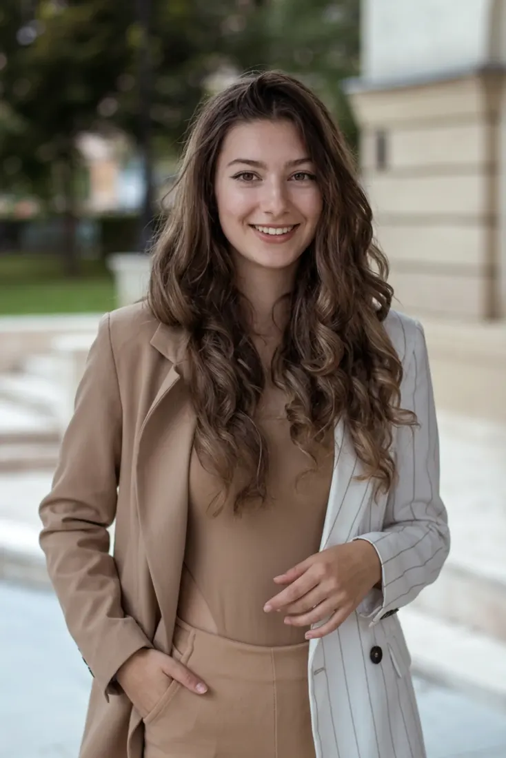 A woman smiles in a beige and white-striped blazer outdoors, before the Spotlight Portrait Generator restyles the portrait.
