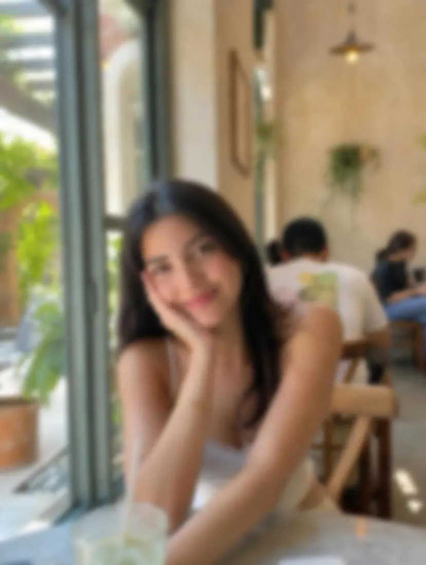 A woman resting her chin on her hand at a cafe appears blurry and out of focus, before the Unblur Image tool.